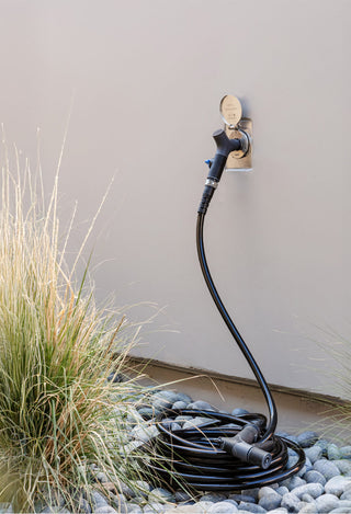 Installed slate gray house hydrant v2+ with straight hose connector and hose on white lap siding and mounting block.