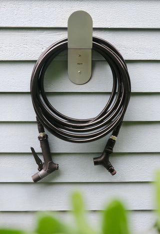 A sage green garden hose sitting against a white wall on green turf grass.