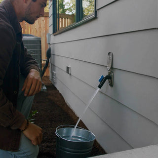 A man watching as a jet black removable faucet connector plugged into a brushed stainless house hydrant v2+ fills up a stainless steel bucket.