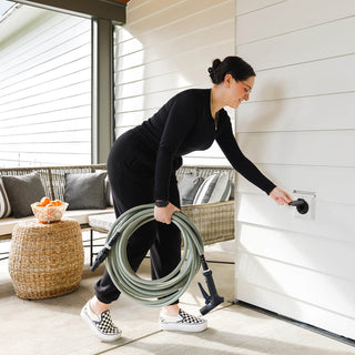 Woman connecting to Matte Black House Hydrant V1+ with wide grip hose connector and sage green ultralight garden hose.