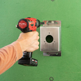 A hand using a power drill to secure the stainless steel mounting box v1+ to sheathing with screws.