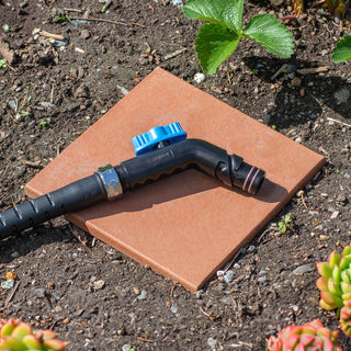A jet black removable faucet hose connector and hose in a garden.