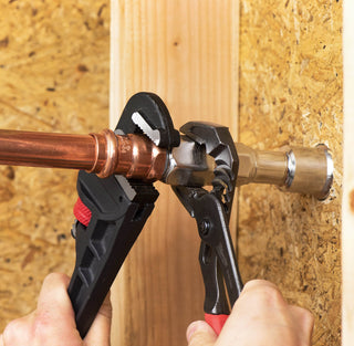 Two hands tightening the connections between the three-quarters inch NPT inlet and copper pipe plumbing with two wrenches.