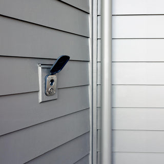 A slate gray house hydrant v2+ with the cover opened on the gray lap siding of a home.