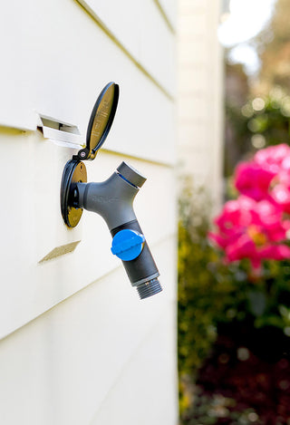 Matte black house hydrant v1+ installed on white lap siding with a comfort grip vb hose connector plugged in.