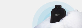 A matte black v2+ house hydrant sitting in some snow with decorative blue circles behind both.