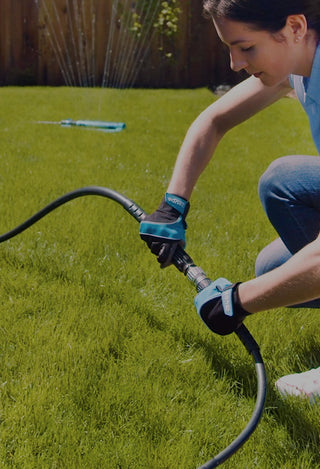 A woman wearing utility gloves connecting hose adapter to turn on sprinkler.