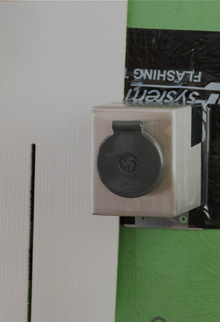 A stainless steel mounting box V1+ with a house hydrant v1+ installed onto sheathing, weatherproofed with zip system flashing. A board is held up to display what siding might look like.