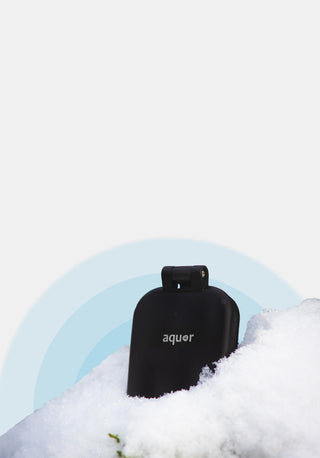A matte black v2+ house hydrant sitting in some snow with decorative blue circles behind both.