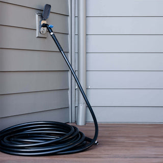 Jet black ultralight garden hose connected to a removable faucet hose connector inserted into a slate gray house hydrant v2+ on gray lap siding.