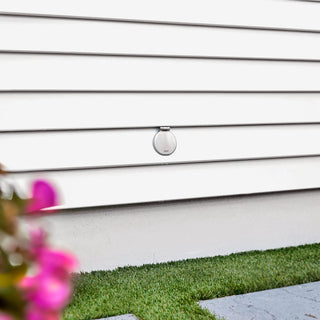 The brushed stainless house hydrant v1+ with a closed cover on white lap siding.