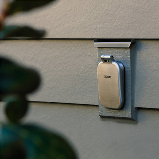 A brushed stainless v2+ debris cover shown on gray lap siding.