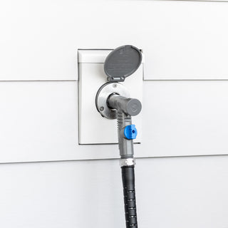 A slate gray vacuum breaker hose connector plugged into a slate gray v1+ house hydrant installed on white lap siding with a white mounting block.