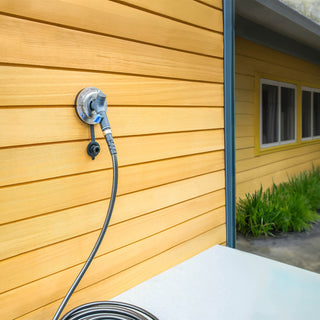 A Hot and Cold Hydrant installed with a connector and hose on the side of a home.
