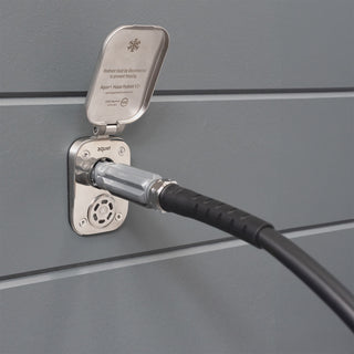 A brushed stainless house hydrant v2+ with a connector and hose inserted, installed on gray lap siding.