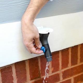 The comfort grip vb hose connector plugged into a house hydrant v1+ with a matte white cover, a man turns the dial and water is coming out of the connector.