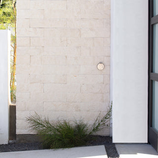 The brushed stainless house hydrant v1+ on stone siding with the cover closed.