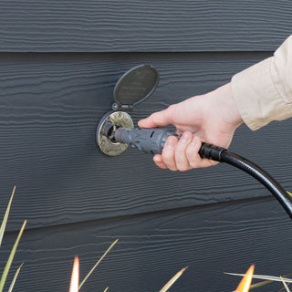 The Slate Gray House Hydrant V1+ installed in dark gray lap siding and a hand in the process of inserting a connector and hose into the hydrant.