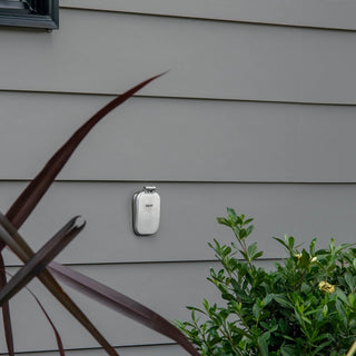 A brushed stainless v2+ debris cover shown on gray lap siding.