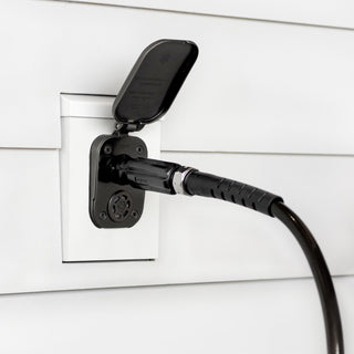 A matte black house hydrant v2+ with a connector and hose inserted, installed on white lap siding with a mounting block.