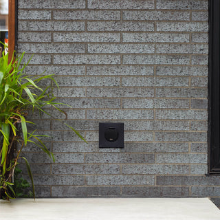 A front facing view of the matte black house hydrant v1+ installed on brick with the cover closed.