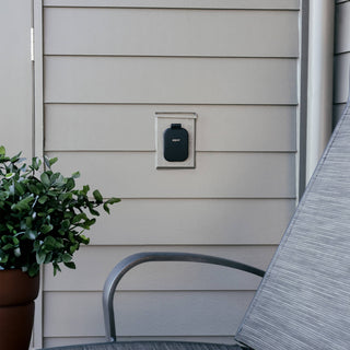 A matte black house hydrant v2+ with the cover closed on the gray lap siding of a home.