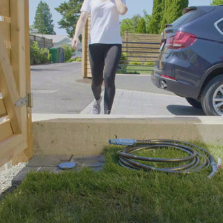 Woman walking towards ground hydrant, picking up hose connector, plugging in, then washing her car.