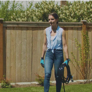 A woman carrying a jet black garden hose. 