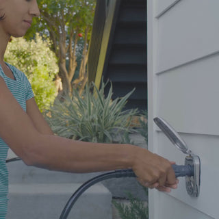A woman plugs in the straight hose connector and hose into the brushed stainless house hydrant v2+ as kids run around in the background.