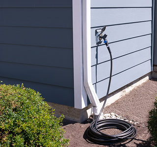 A slate gray house hydrant v1+ installed on lap siding with a comfort grip connector and hose attached.